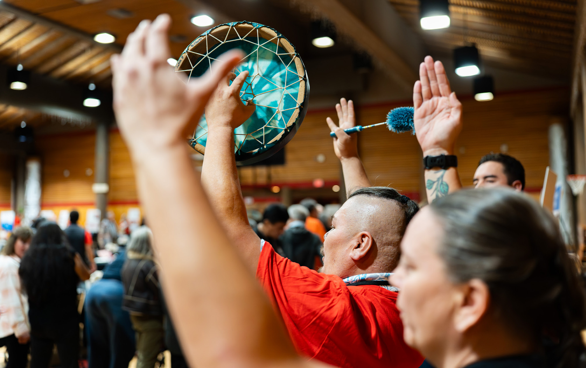 Sḵwx̱wú7mesh community members raising hands and a drum at a Nation gathering